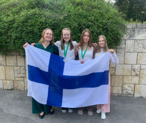 Neljä teinityttöä pitelee Suomen lippua, kahdella kaulassa mitalit.