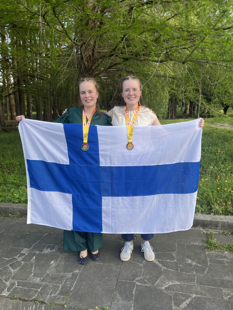 Aino ja Siiri mitalit kaulassaan pitelevät Suomen lippua